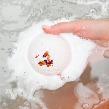 Bathorium Mama’s Perch bath bomb dissolving in water with rose petals, coconut milk, and frothy bubbles.