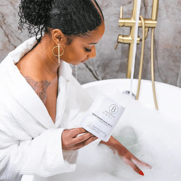 Bathorium Northern Sage Recovery bath soak held by a woman in a white robe over a steaming bathtub