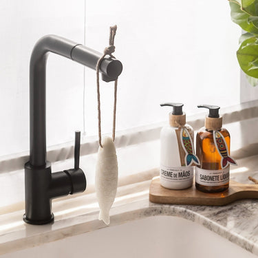 Kindred & Kin Castelbel  Sea Salt & Lemon sardine-shaped soap on a rope hanging by a black kitchen faucet.