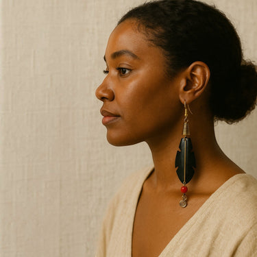 Kindred & Kin Sutura Feather Drop Earrings: black bone feather with brass wirework, coral bead, and spiral detail.