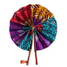Kindred & Kin African print folding fan with purple, red, yellow, and turquoise patterns. Features leather-wrapped handles.