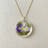 Kindred & Kin Belart Full-Moon Larkspur necklace featuring purple and white pressed flowers in clear resin on a gold chain.
