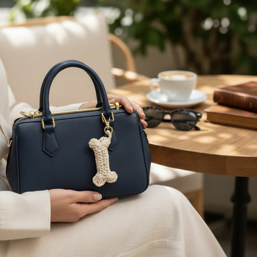 Kindred & Kin hand-crocheted natural raffia dog bone bag charm clipped to a navy blue leather handbag