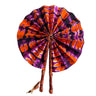 Kindred & Kin foldable fabric fan with tie-dye pattern in orange, purple, and black, featuring leather-wrapped handles.